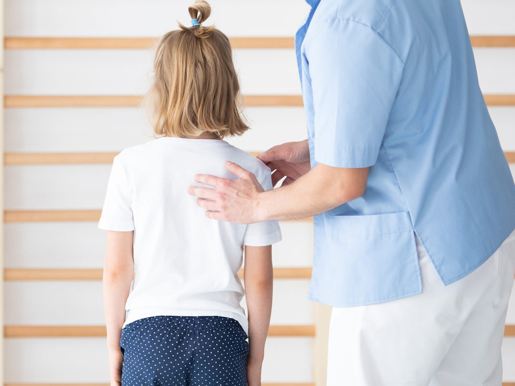 dr examine a young girls not aligned shoulder due to scoliosis