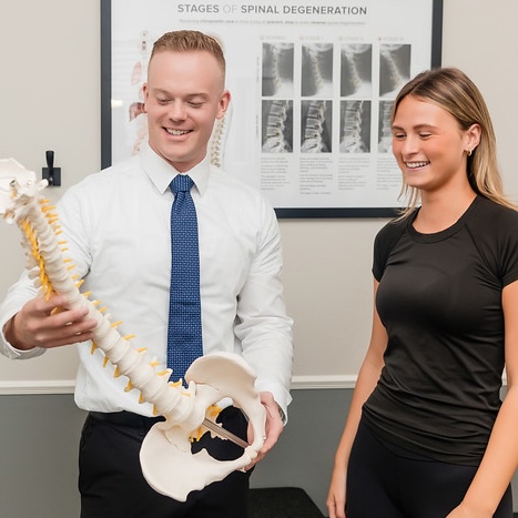 dr. Henricksen spine model to a smiling woman in black athletic wear
